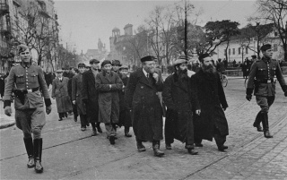 Żydzi eskortowani w drodze do pracy na Krakowskim Przedmieściu (marzec 1940) [fot. wikipedia/domena publiczna]